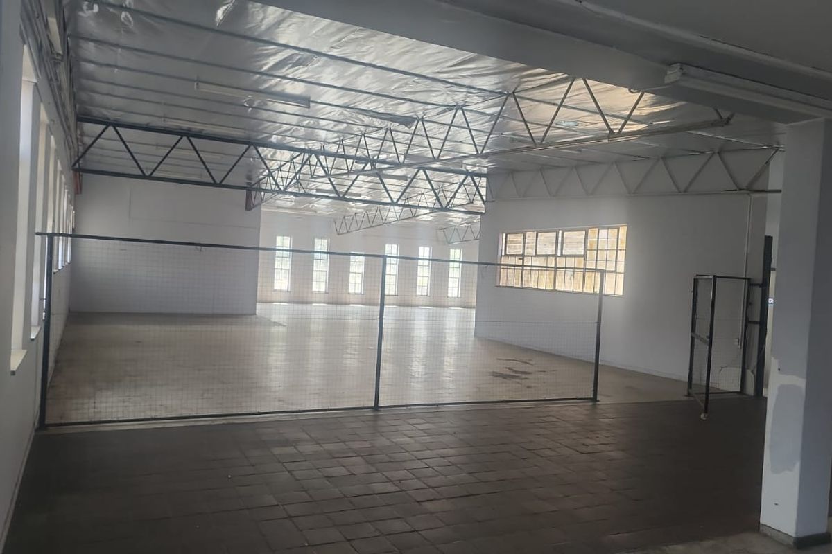 Spacious industrial utility area featuring exposed steel roof trusses, tiled flooring, and large windows, offering a versatile open-plan layout for various commercial uses.