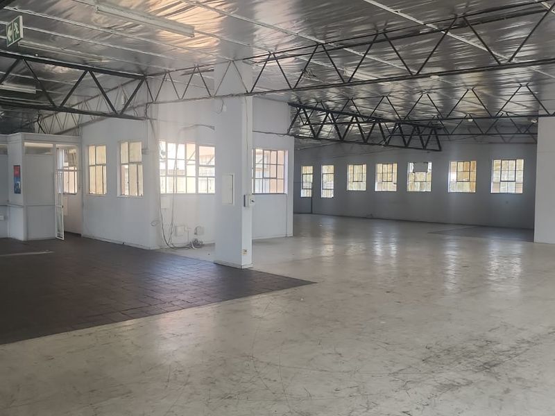Spacious open-plan industrial warehouse area featuring exposed steel roof trusses, reflective insulation, concrete flooring, and a partitioned office enclosure.