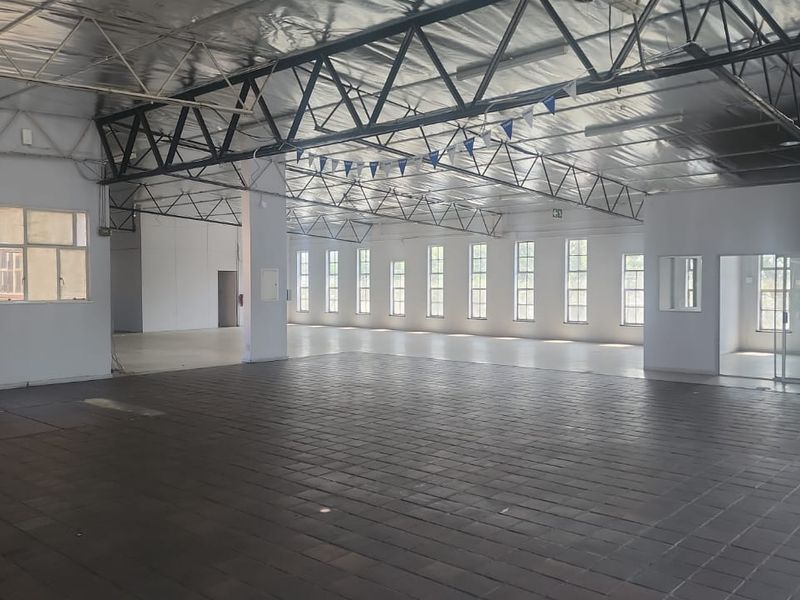 Spacious open-plan industrial warehouse area featuring exposed steel roof trusses, reflective insulation, tiled flooring, and abundant natural light through steel-framed windows.