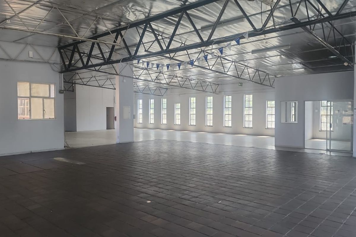 Spacious open-plan industrial warehouse area featuring exposed steel roof trusses, reflective insulation, tiled flooring, and abundant natural light through steel-framed windows.
