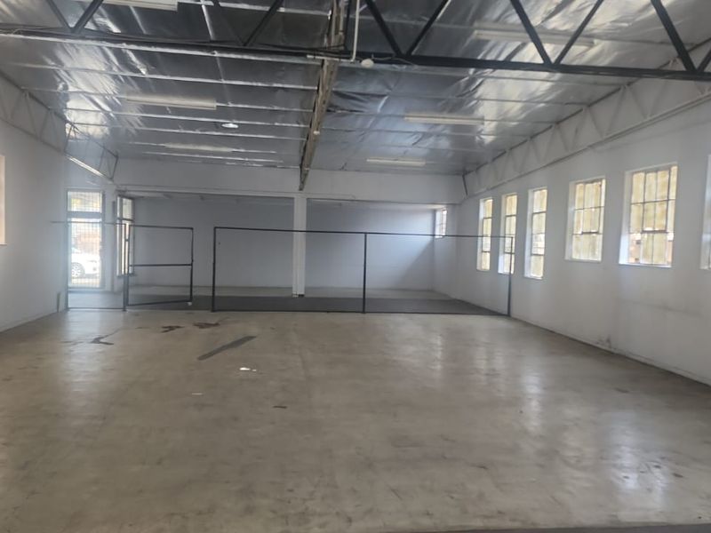 Spacious industrial utility area featuring exposed steel roof trusses, reflective insulation, concrete flooring, and multiple steel-framed windows providing ample natural light.
