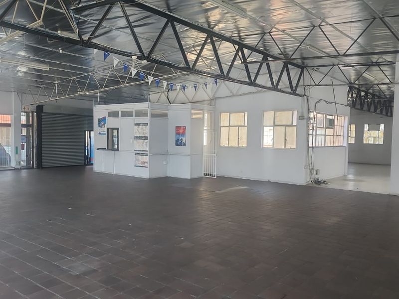 Spacious open-plan industrial unit featuring exposed steel roof trusses, tiled flooring, a partitioned office area, and a secure roller shutter door.