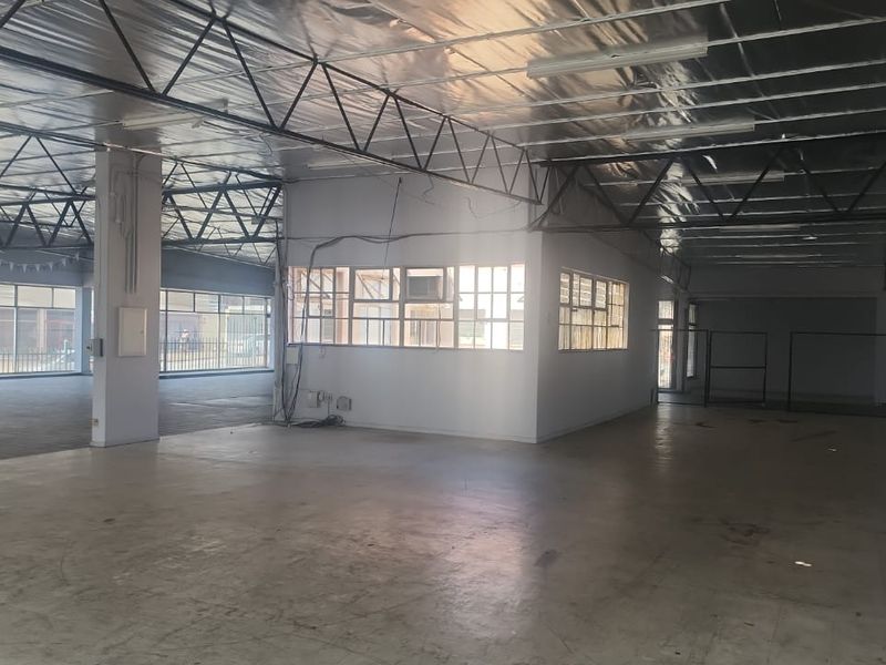Spacious open-plan industrial unit featuring exposed steel roof trusses, reflective insulation, concrete flooring, and a central partitioned office area with large windows.