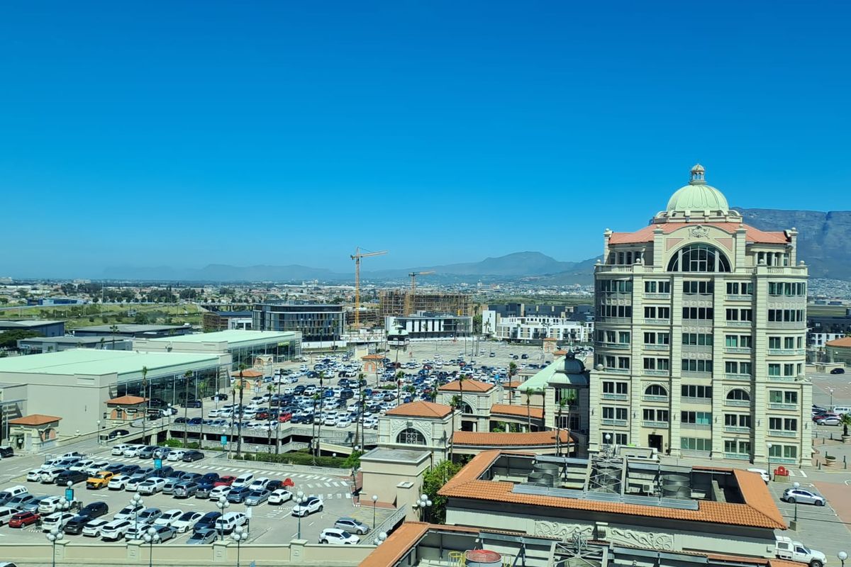 Elevated aerial view overlooking a commercial office complex, parking areas, and surrounding urban landscape with mountain views in the distance.