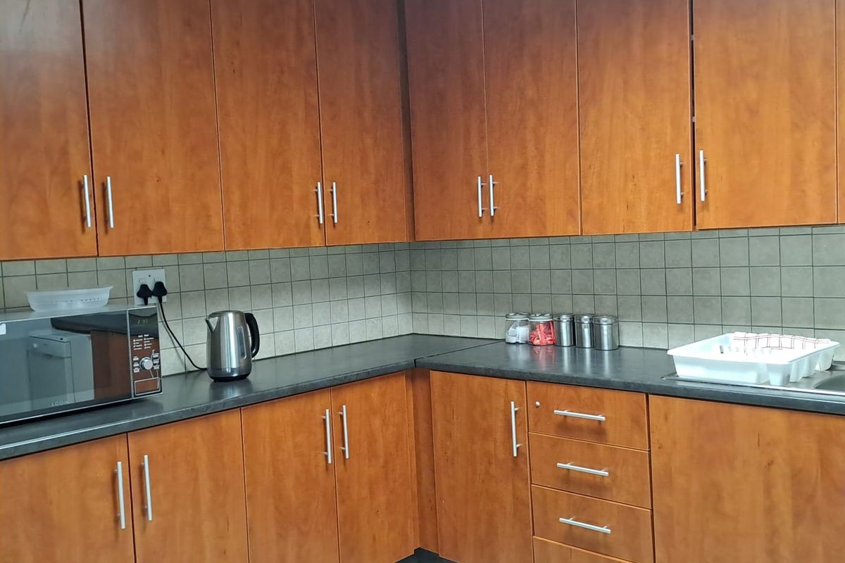 A functional office kitchenette featuring wood-look cabinetry, dark laminate countertops, and tiled backsplash, providing essential workspace for staff.