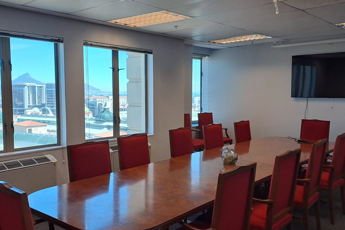 A professional boardroom featuring a large wooden conference table, suspended ceiling grid with integrated lighting, and large windows offering city views.