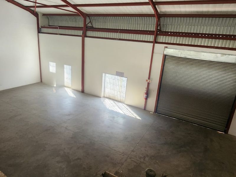 Spacious industrial warehouse unit featuring high ceilings, exposed steel structure, concrete flooring, and a large roller shutter door for easy access.