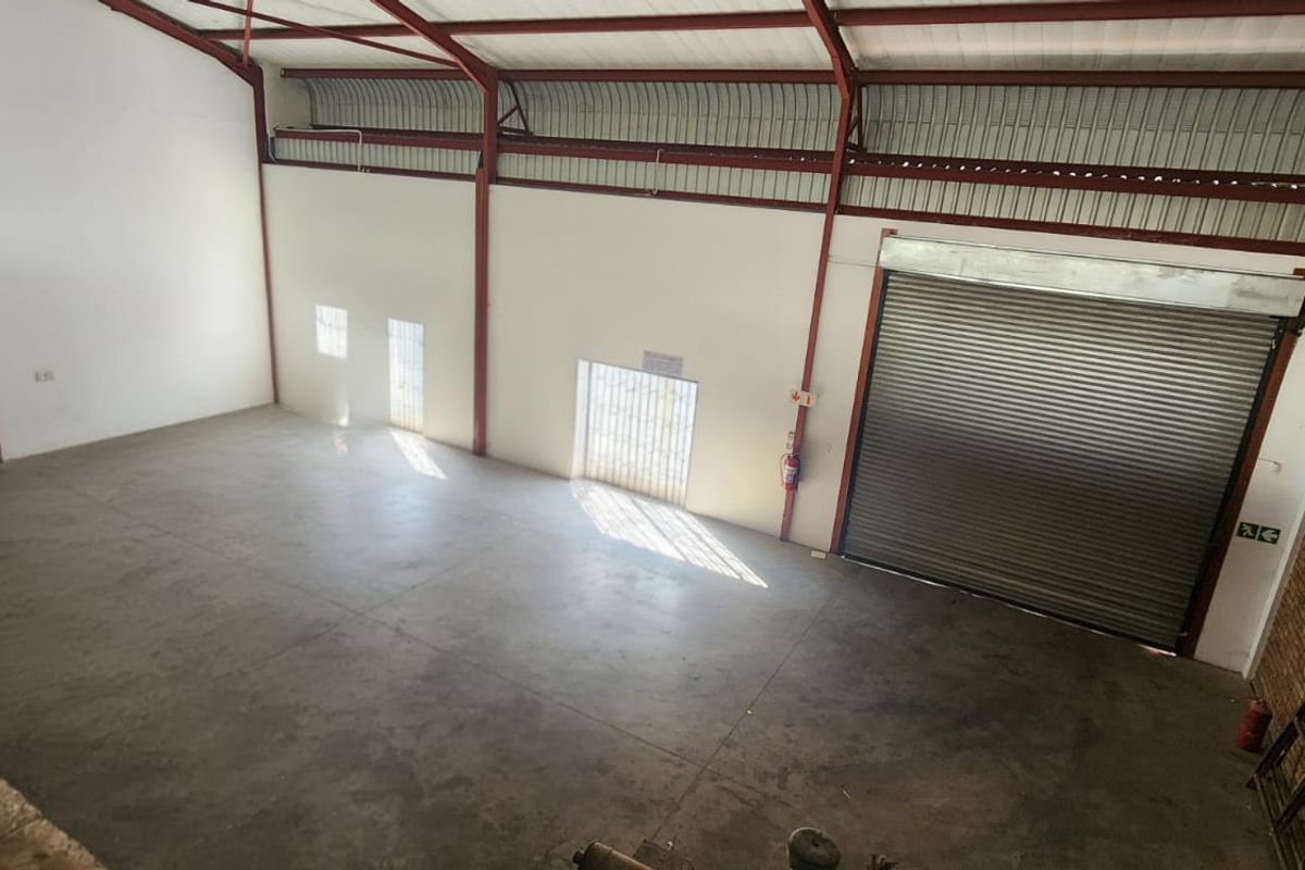 Spacious industrial warehouse unit featuring high ceilings, exposed steel structure, concrete flooring, and a large roller shutter door for easy access.