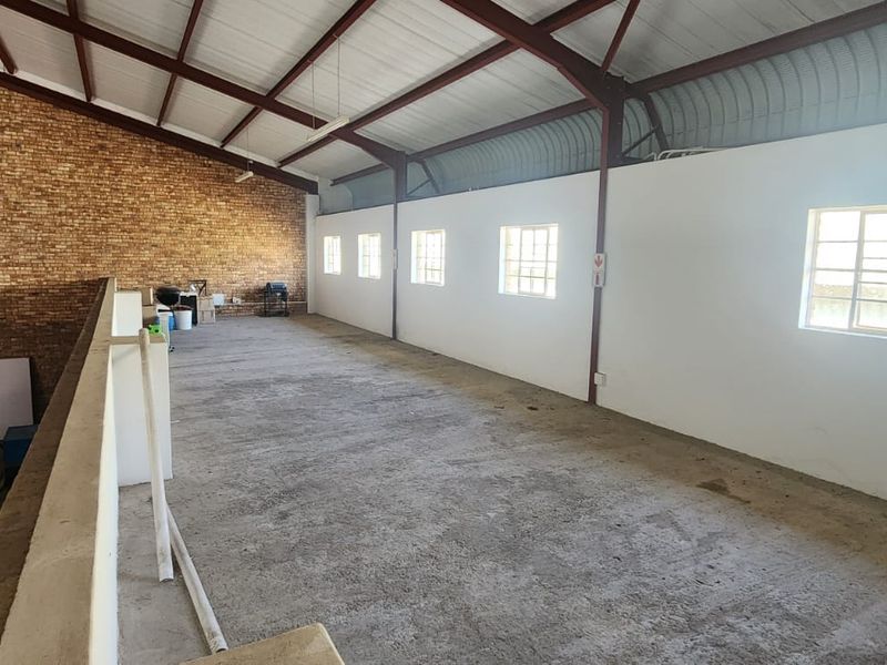 Spacious industrial mezzanine level featuring exposed brickwork, steel roof trusses, and concrete flooring, suitable for storage or flexible workspace use.