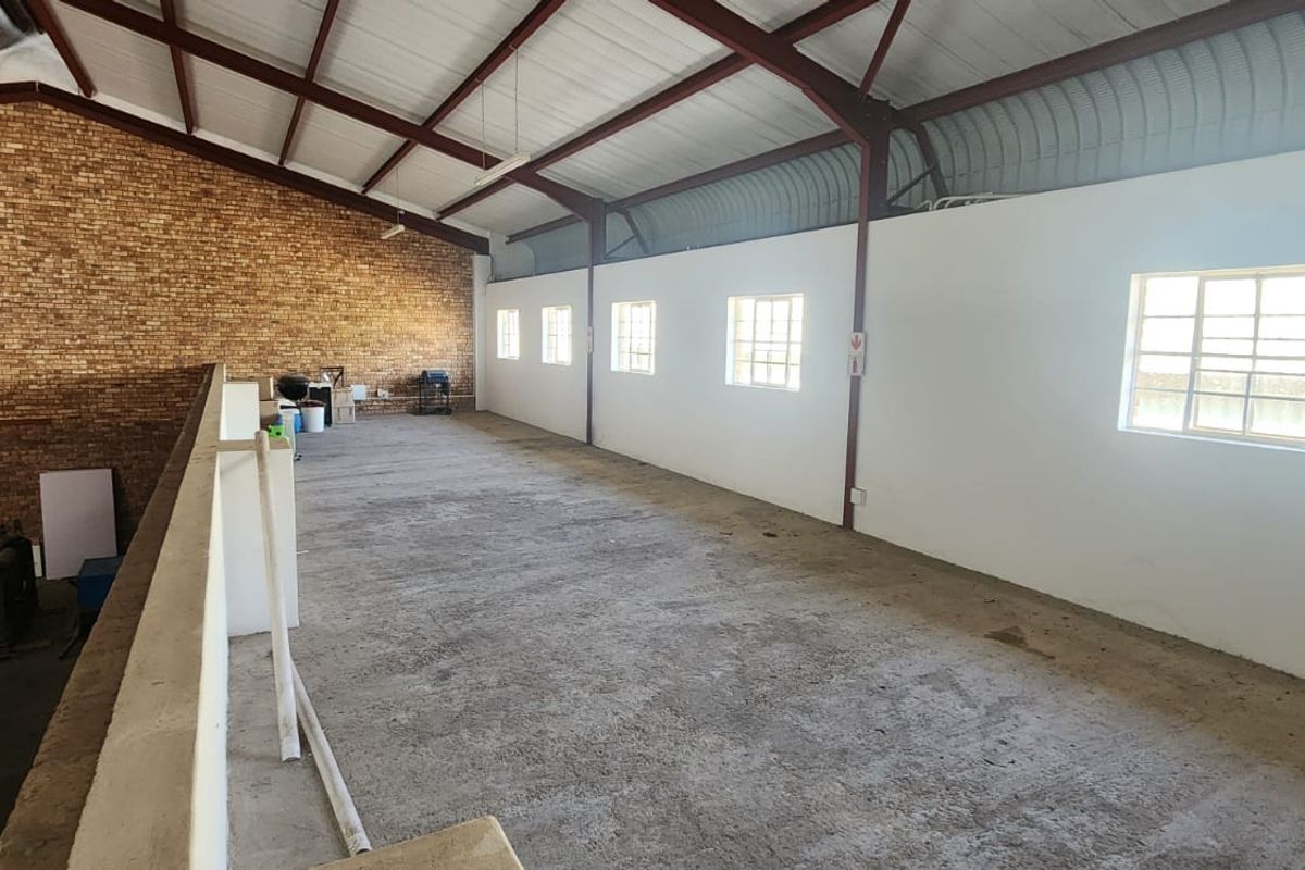 Spacious industrial mezzanine level featuring exposed brickwork, steel roof trusses, and concrete flooring, suitable for storage or flexible workspace use.