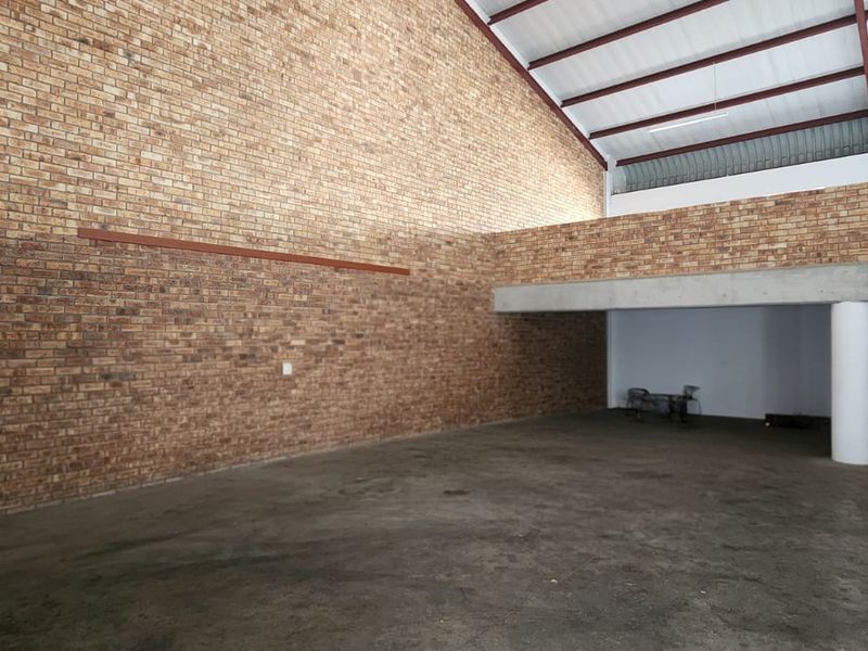 Spacious industrial utility area featuring exposed brick walls, concrete flooring, and a mezzanine level with exposed steel roof trusses.