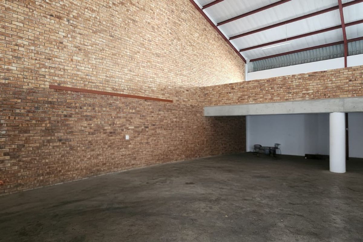 Spacious industrial utility area featuring exposed brick walls, concrete flooring, and a mezzanine level with exposed steel roof trusses.