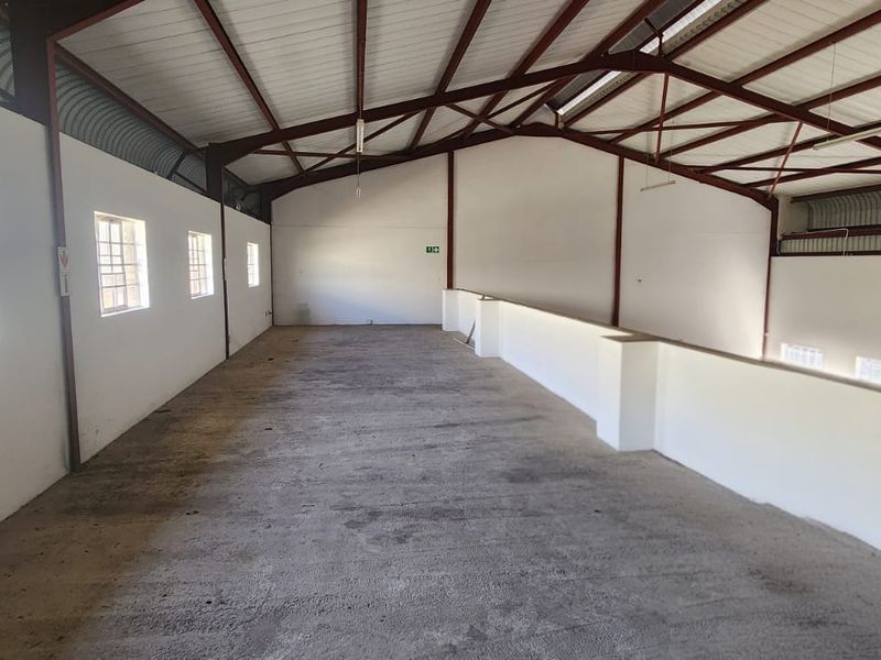 Spacious industrial mezzanine area featuring exposed steel roof trusses, concrete flooring, and natural light from multiple steel-framed windows.