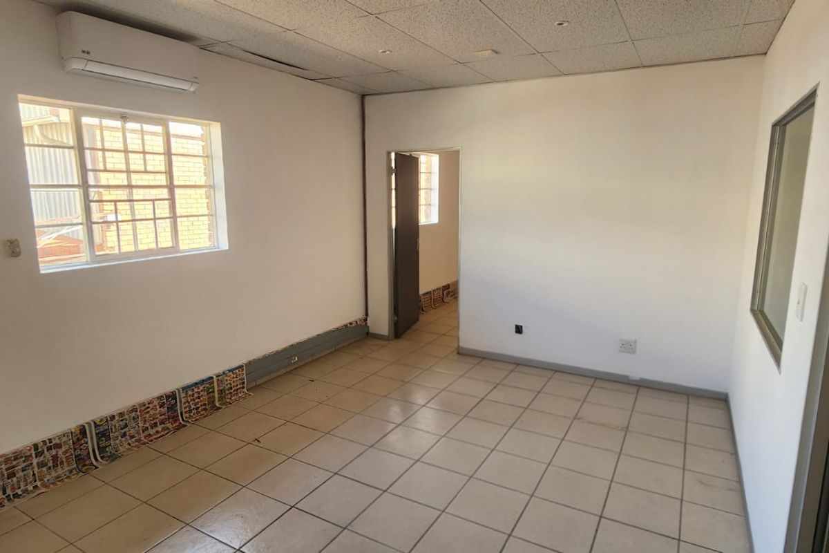 An empty office space featuring tiled flooring, a wall-mounted air conditioning unit, and a window with security bars.