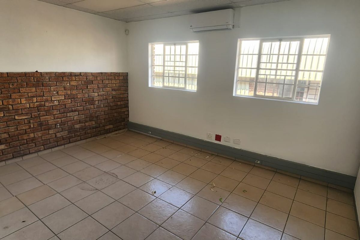 An empty office space featuring tiled flooring, a decorative brick accent wall, security bars on windows, and a wall-mounted air conditioning unit.