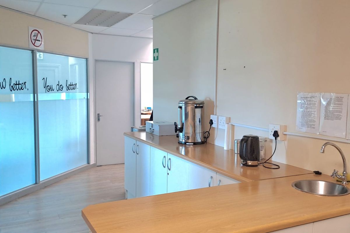 A functional office kitchenette featuring laminate countertops, built-in cabinetry, a stainless steel sink, and a suspended ceiling with integrated lighting.