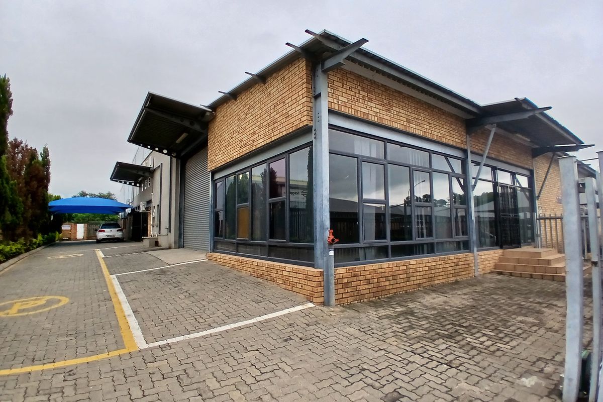 Commercial property featuring a modern face brick facade, large glass windows, steel structural elements, and a paved driveway with designated parking.