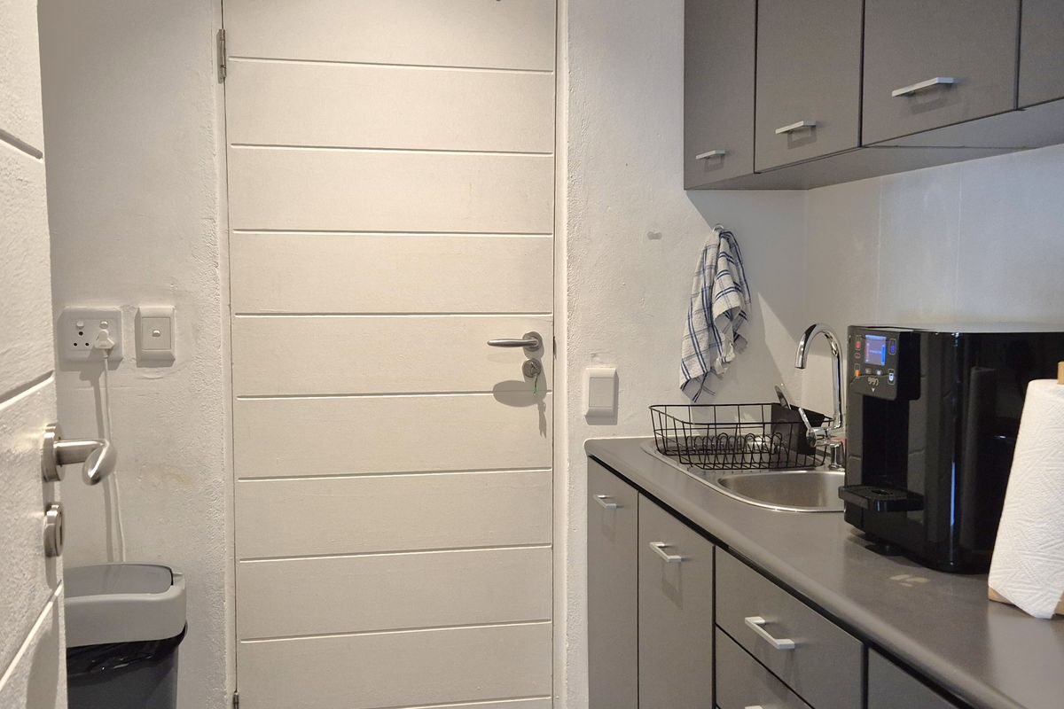 A compact office kitchenette featuring grey cabinetry, a stainless steel sink, and a modern horizontal-panel door.
