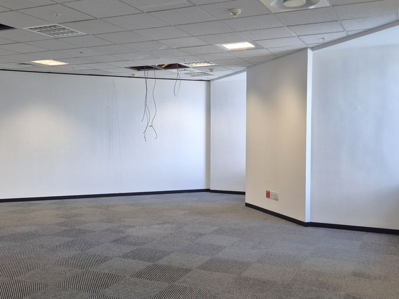 An empty, open-plan office space featuring carpet tiles, a suspended ceiling with recessed lighting, and exposed wiring requiring maintenance.