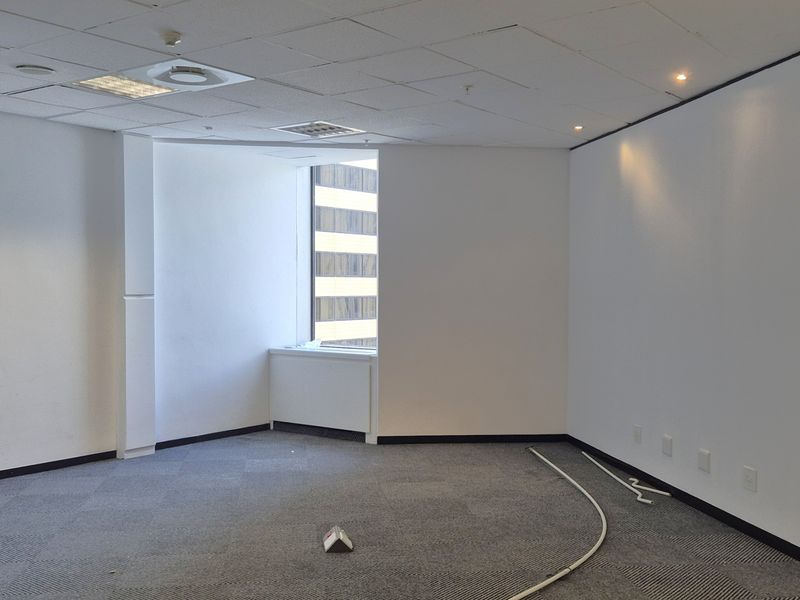 An empty, open-plan office space featuring carpeted flooring, a suspended ceiling with recessed lighting, and integrated electrical and data connectivity.