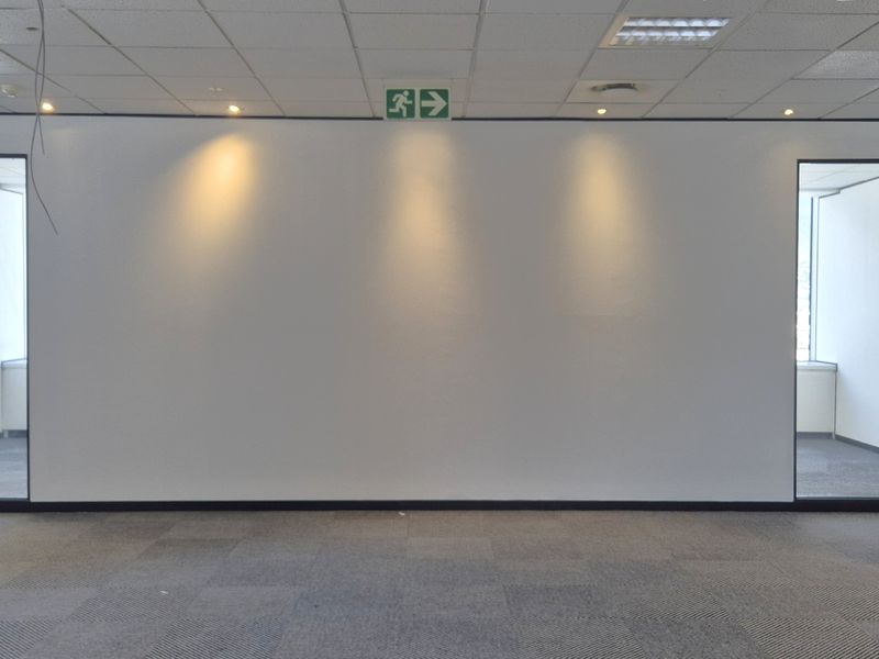 An empty, open-plan office space featuring carpeted flooring, a suspended ceiling with recessed lighting, and glass-partitioned doorways.