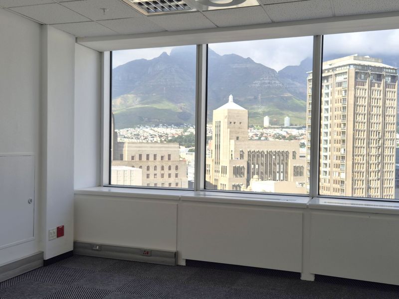 A bright, empty office space featuring large windows with expansive city and mountain views, carpeted flooring, and integrated perimeter electrical trunking.