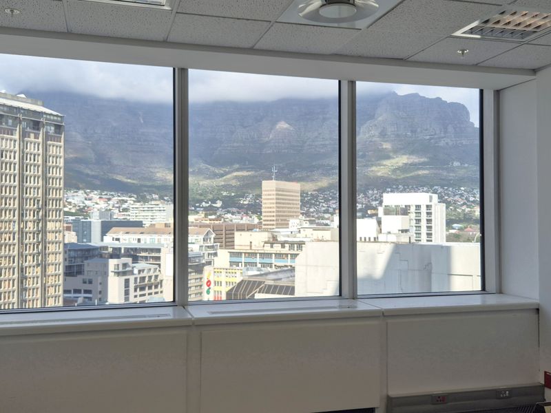 A bright, empty office space featuring large windows with expansive city and mountain views, suspended ceilings, and integrated lighting.