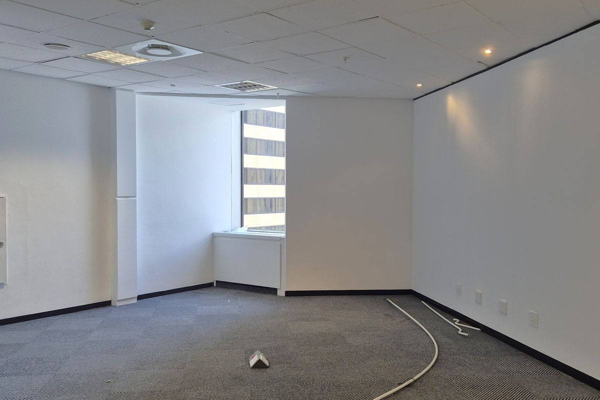 An empty, open-plan office space featuring carpeted flooring, a suspended ceiling with recessed lighting, and integrated electrical and data connectivity.