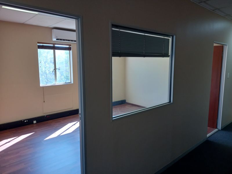 A vacant office space featuring laminate flooring, a split-system air conditioner, and an internal glass partition window providing natural light.