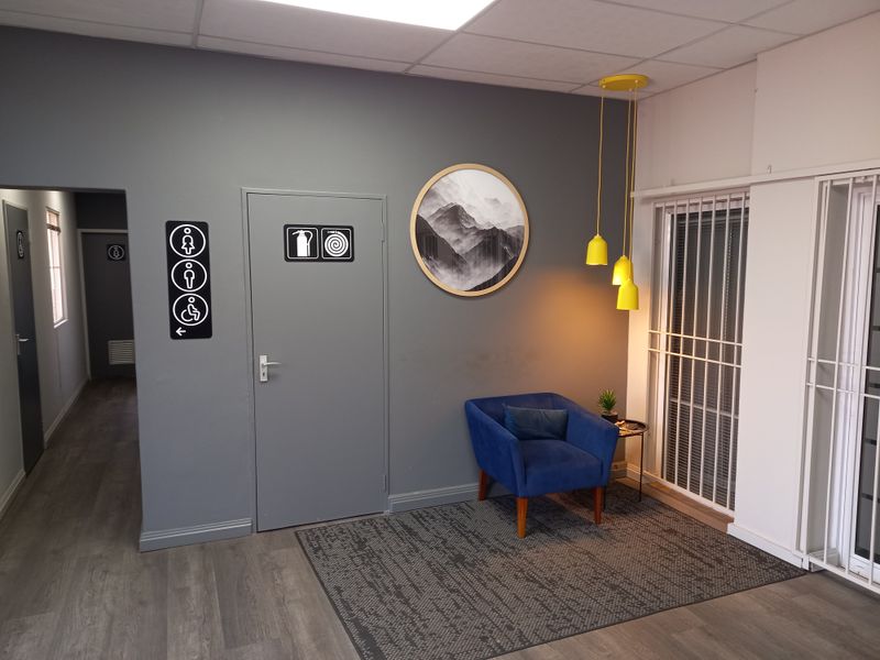 A modern office waiting area featuring grey walls, laminate flooring, suspended ceiling, and clear directional signage for facilities.
