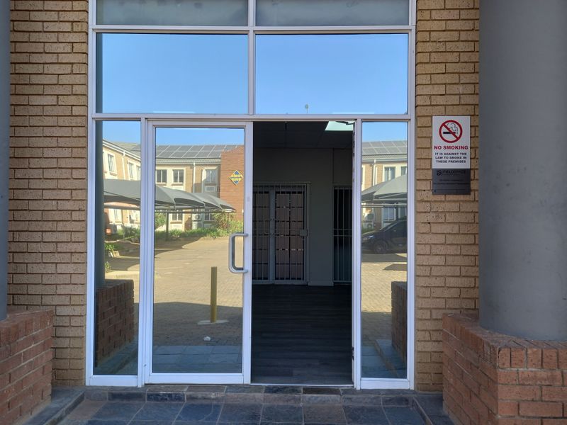 Office building entrance featuring a glass door, brick facade, and secure internal gate access.