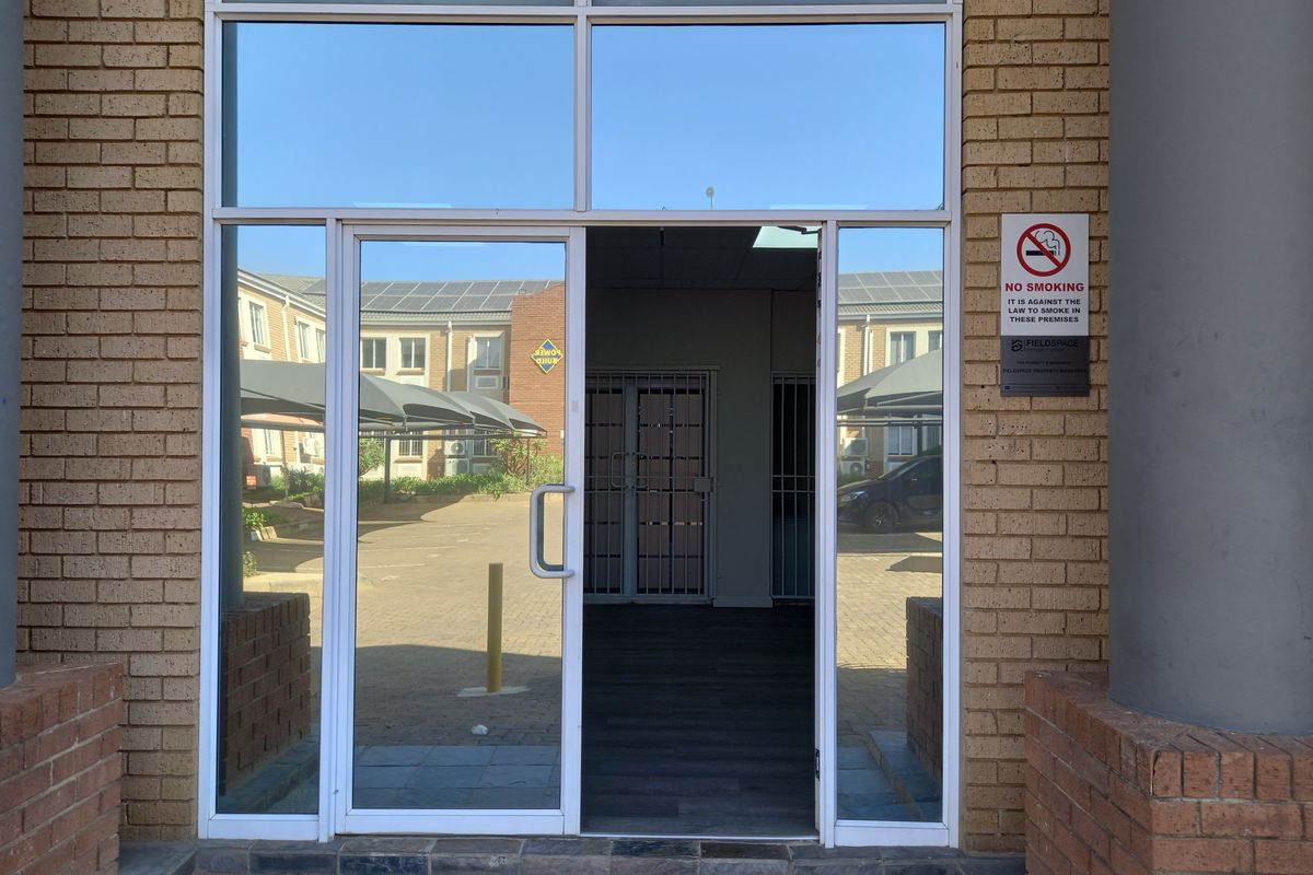 Office building entrance featuring a glass door, brick facade, and secure internal gate access.