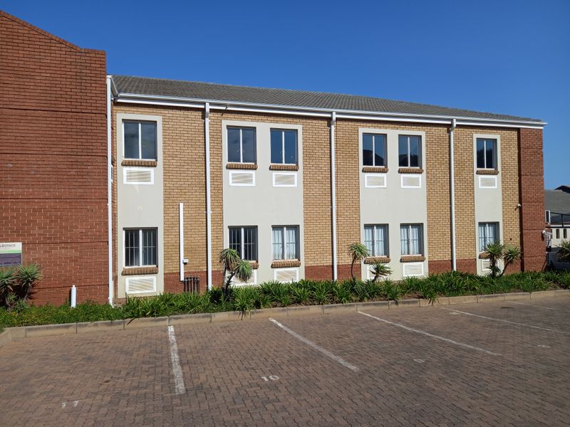 Exterior view of a two-story brick office building featuring a paved parking area, tiled roof, and security-fitted windows.