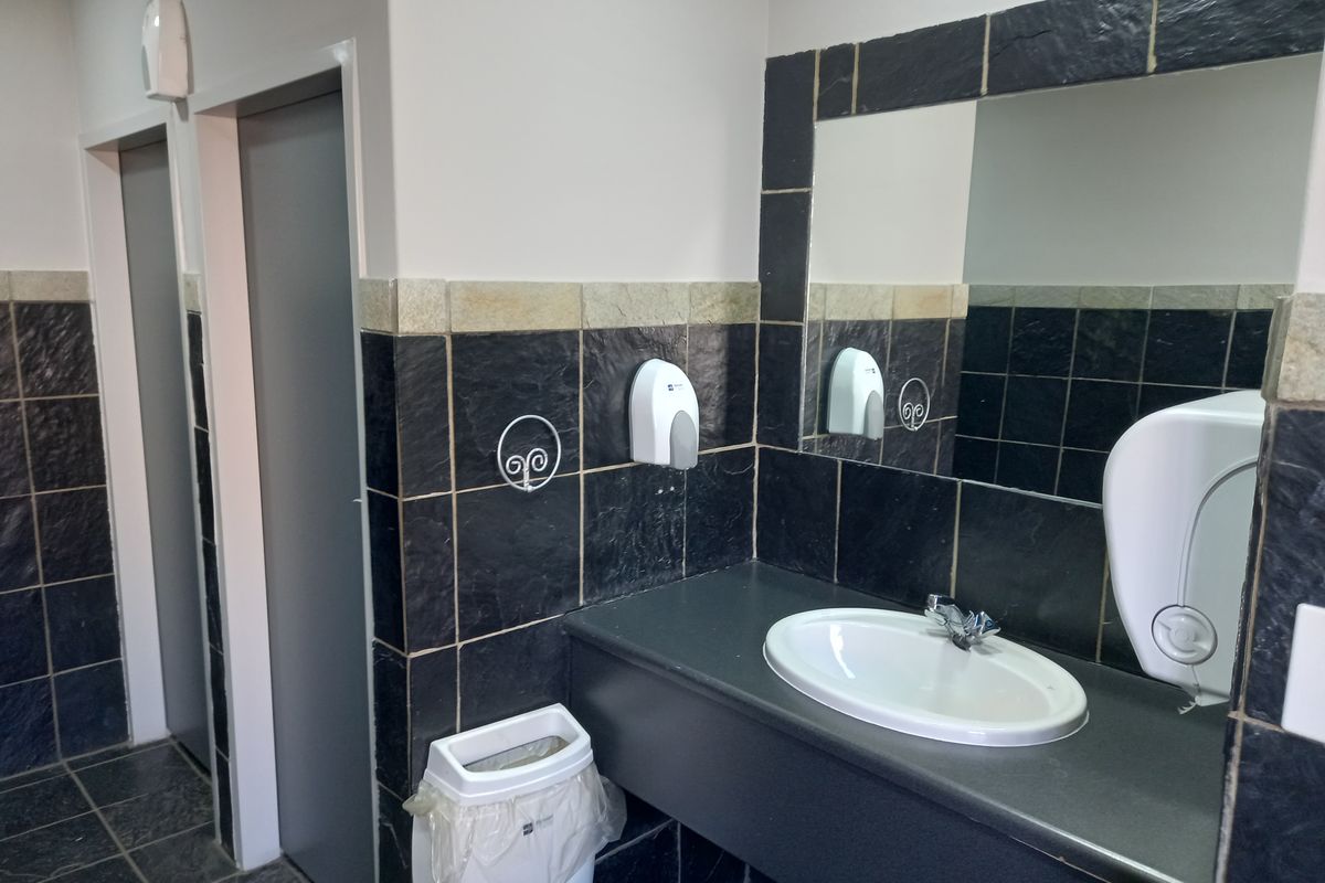 A functional office bathroom featuring a vanity basin, dark tiled walls, and a fitted mirror.