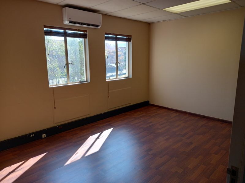 A vacant office space featuring laminate flooring, a suspended ceiling with recessed lighting, and a wall-mounted split-system air conditioning unit.