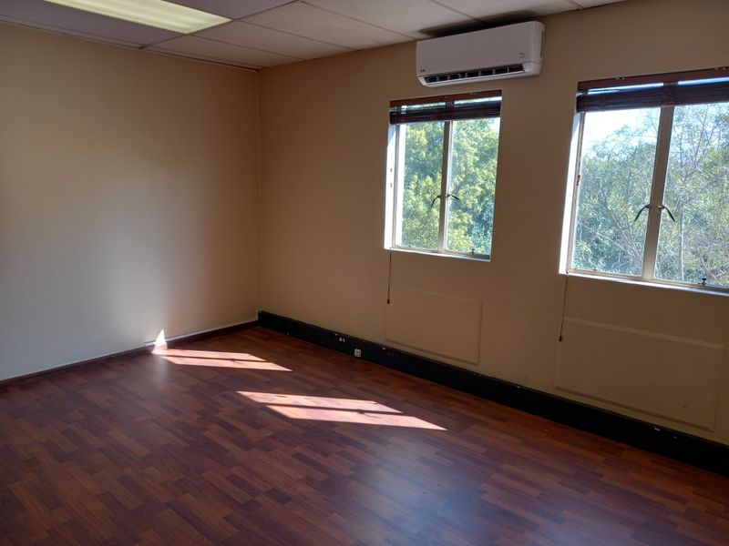 Empty office space featuring laminate flooring, a drop ceiling with integrated lighting, and a wall-mounted split-system air conditioning unit.