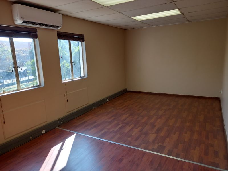 A vacant office space featuring laminate flooring, a suspended ceiling with recessed lighting, and a wall-mounted air conditioning unit.