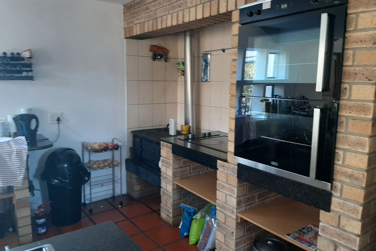 A rustic kitchen area featuring a built-in oven, brick fireplace structure, and tiled flooring, offering a traditional farm-style aesthetic.