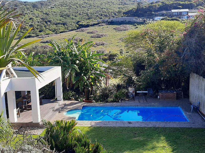 Outdoor entertainment area featuring a swimming pool, covered patio, and landscaped garden with scenic hillside views.