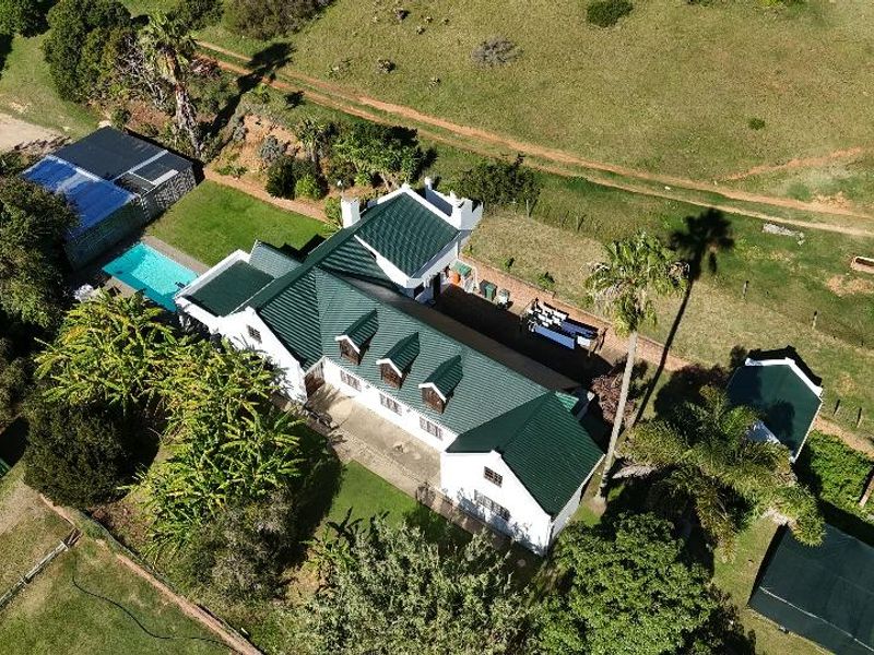 Aerial view of a farm property featuring a main residence with a green pitched roof, a swimming pool, and surrounding landscaped grounds.