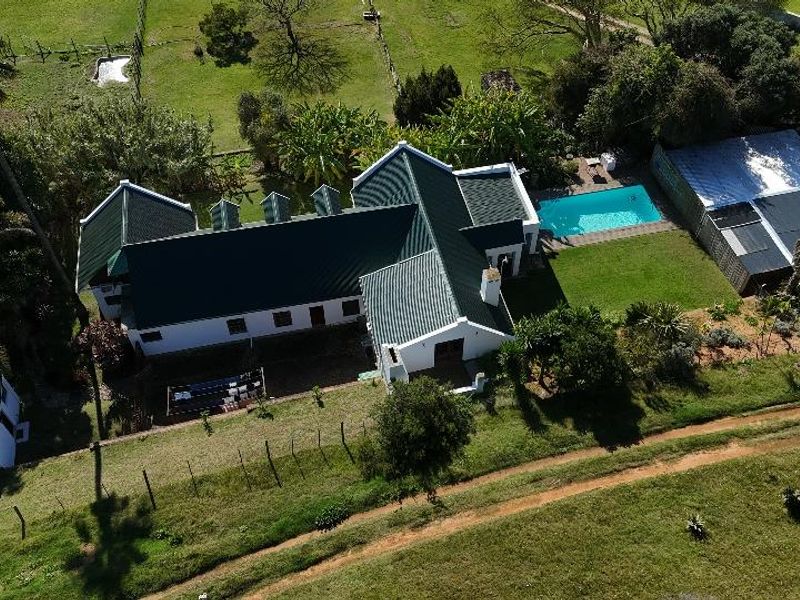 Aerial view of a farm property featuring a main residence with a green metal roof, a swimming pool, and surrounding landscaped grounds.