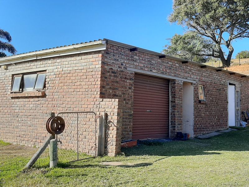 A detached face brick garage building featuring a roller shutter door and casement windows, situated on a grassy farm plot.