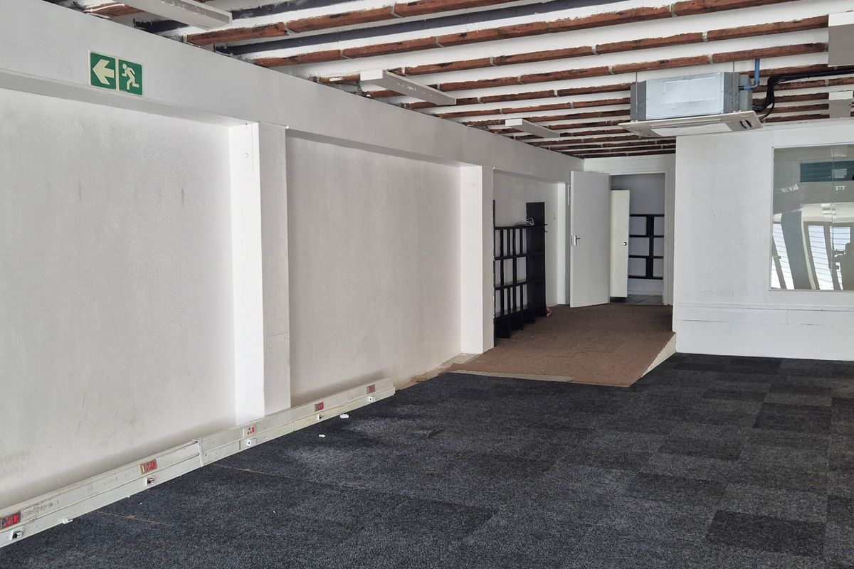 An open-plan commercial retail space featuring exposed ceiling joists, carpet tile flooring, perimeter electrical trunking, and a ducted air conditioning unit.