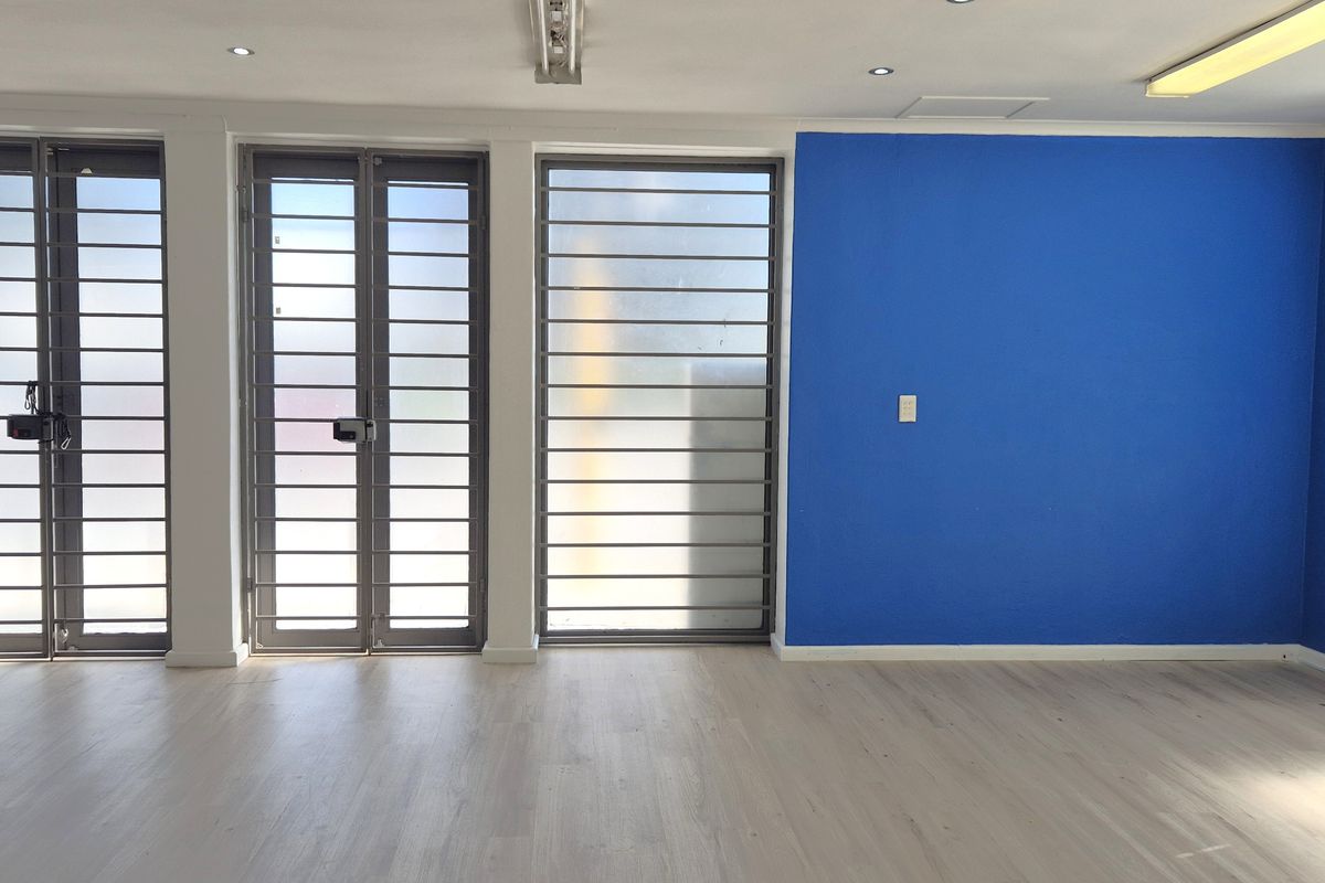 Spacious open-plan retail area featuring light laminate flooring, secure metal gates, and a combination of recessed and fluorescent lighting.