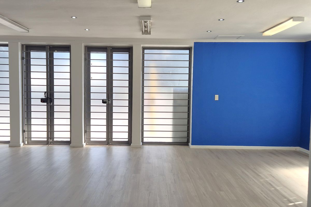 A bright, open-plan retail space featuring light-toned laminate flooring, recessed lighting, and secure metal-framed glass doors.
