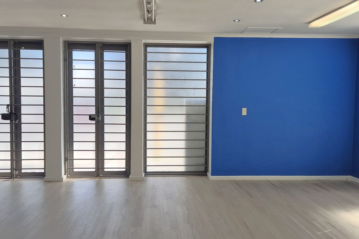 A bright, open-plan retail or office space featuring laminate flooring, secure metal gates, and modern recessed lighting with a bold blue accent wall.