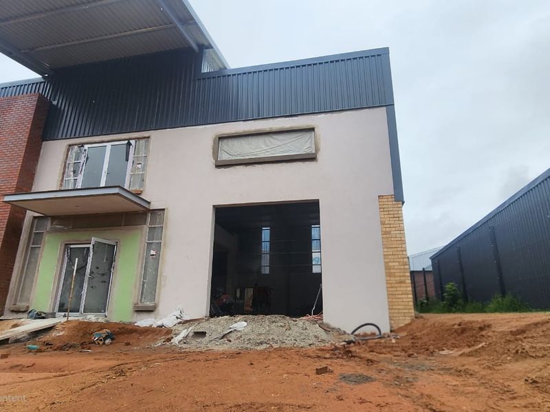 Front elevation of an industrial property under construction, featuring a mix of brick and metal cladding with an open roller shutter entrance.
