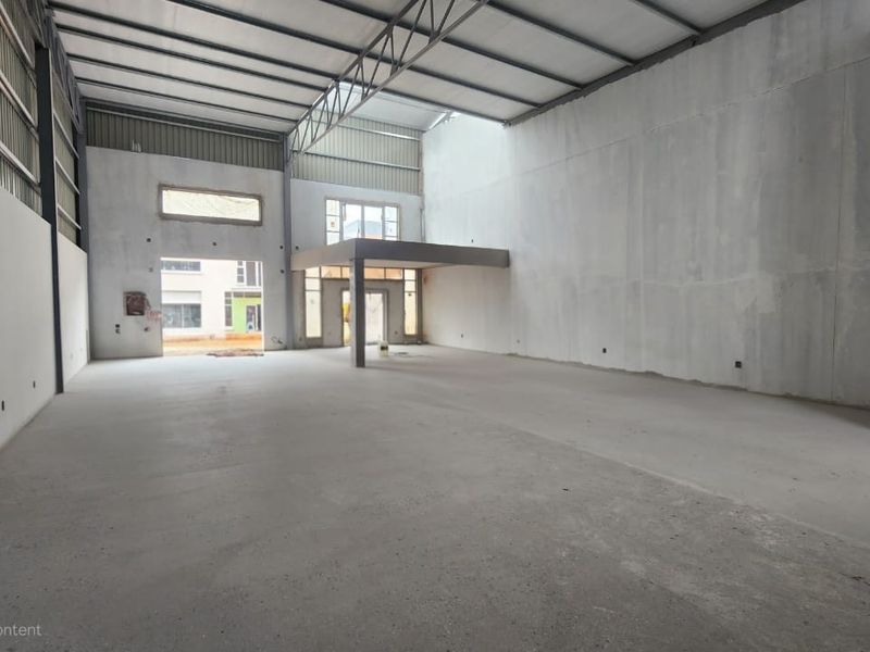 Spacious industrial warehouse unit featuring high ceilings, exposed steel trusses, concrete flooring, and a mezzanine level, currently in an unfinished shell condition.