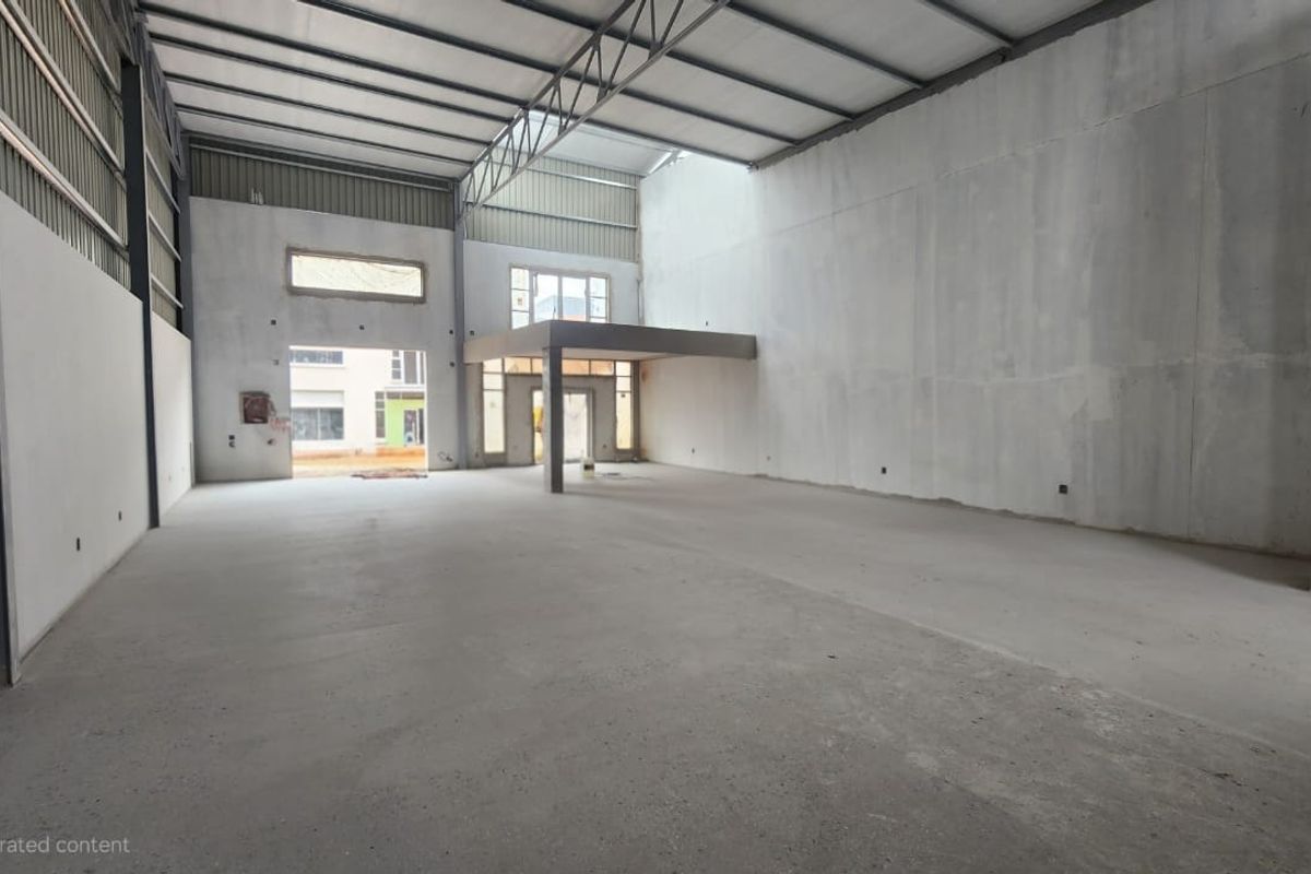 Spacious industrial warehouse unit featuring high ceilings, exposed steel trusses, concrete flooring, and a mezzanine level, currently in an unfinished shell condition.