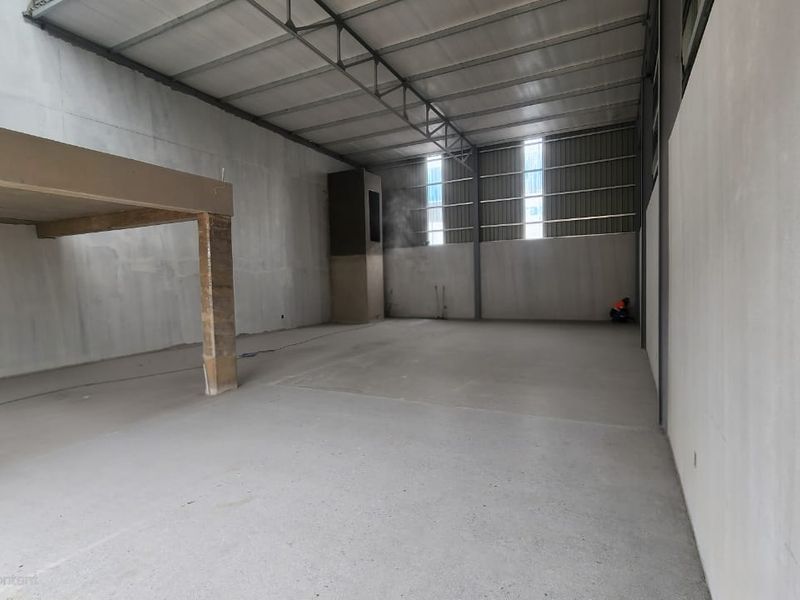 Spacious industrial warehouse unit featuring high ceilings with exposed steel trusses, concrete flooring, and a mezzanine level, offering versatile space for various business operations.